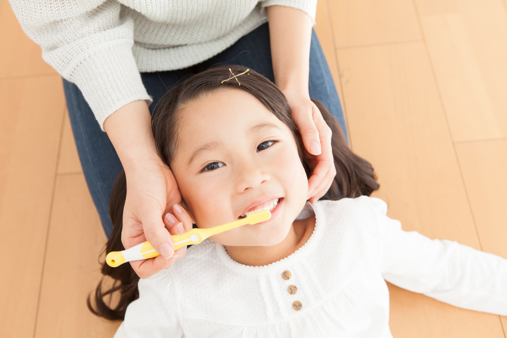 母親の膝枕で仕上げ磨きをしてもらう女の子