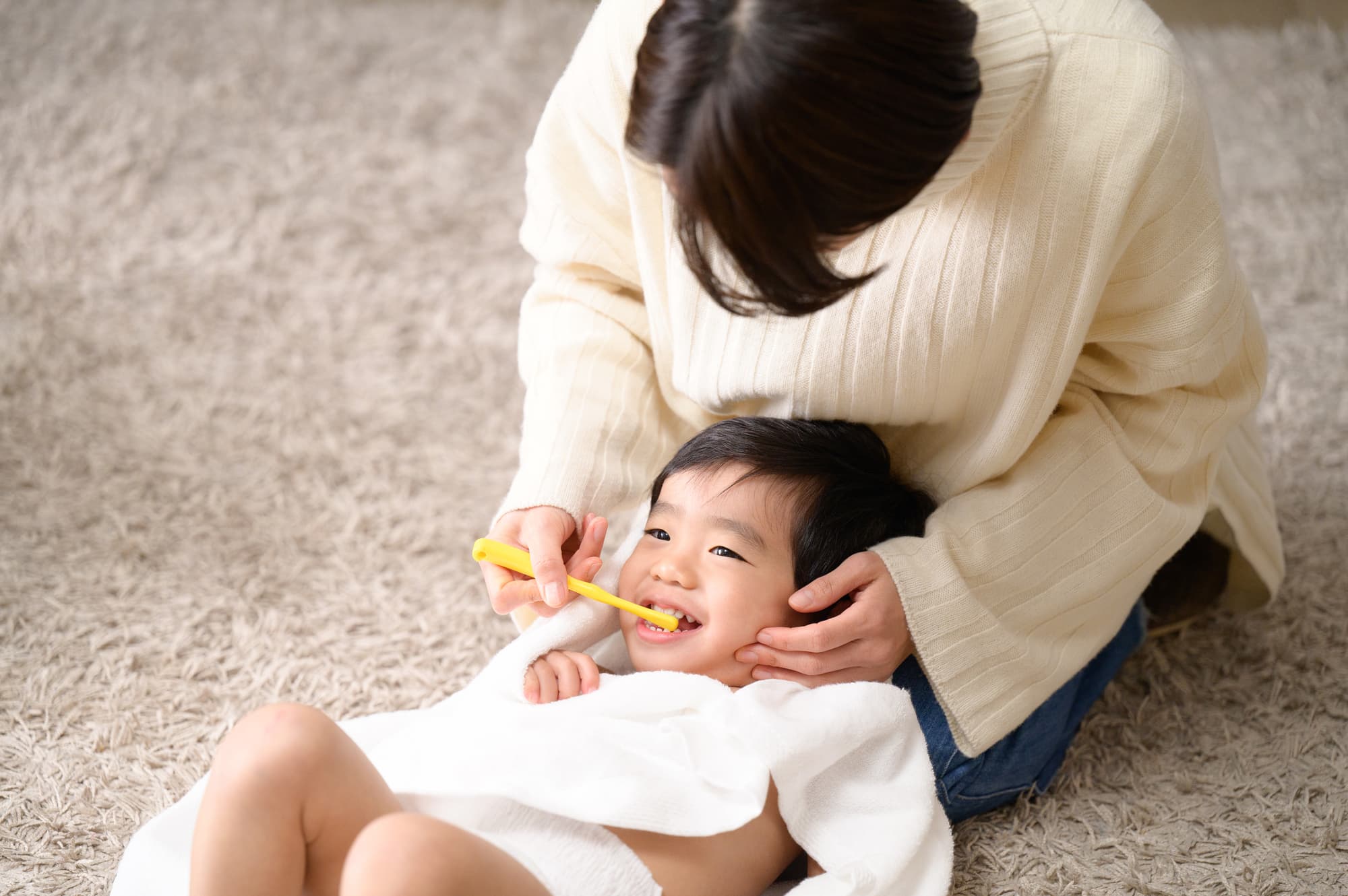 仕上げ磨きをする母と笑顔で磨いてもらっている子ども