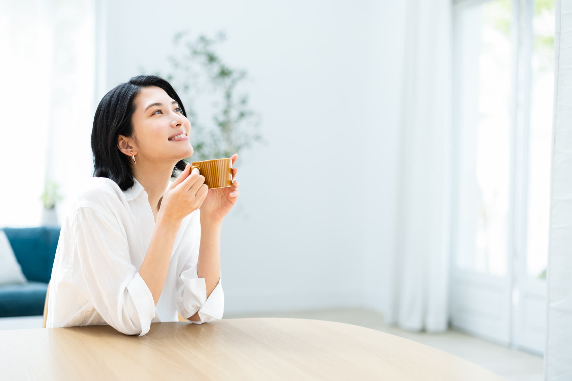 マグカップを両手で持ちリラックスした笑顔の女性