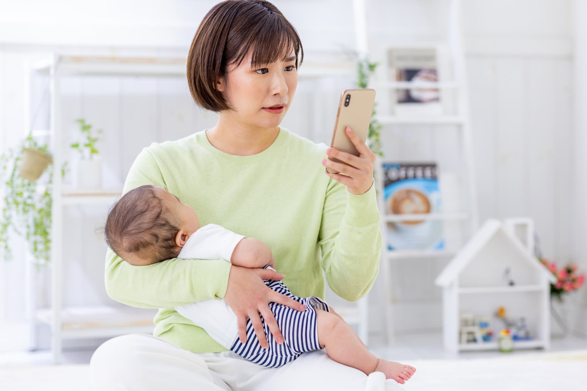 赤ちゃんを抱っこしながら子どもの歯磨きをするときの注意点を調べる母親