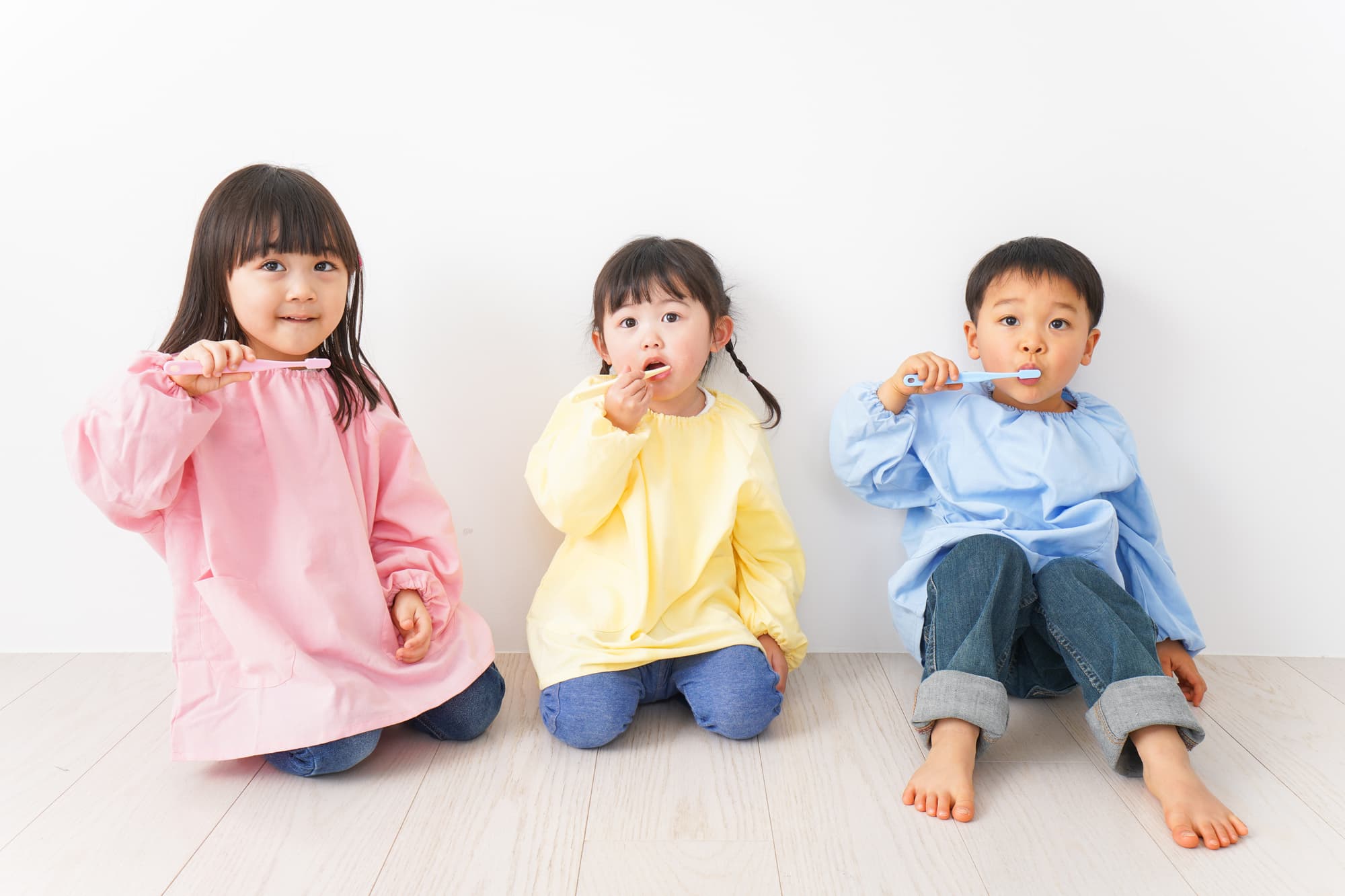 スモックを着て歯磨きする3人の子ども